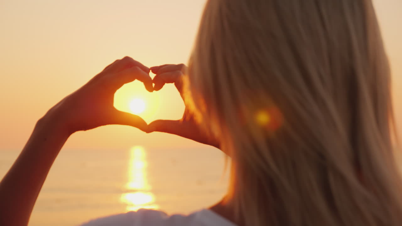 한 여성이 하트 모양으로 손을 잡고 해가 뜨는 바다를 바라본다 사랑과 로마