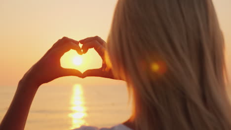 A-Woman-Holds-Her-Hands-In-The-Shape-Of-A-Heart-Looks-At-The-Ocean-Where-The-Sun-Rises-Love-And-Roma