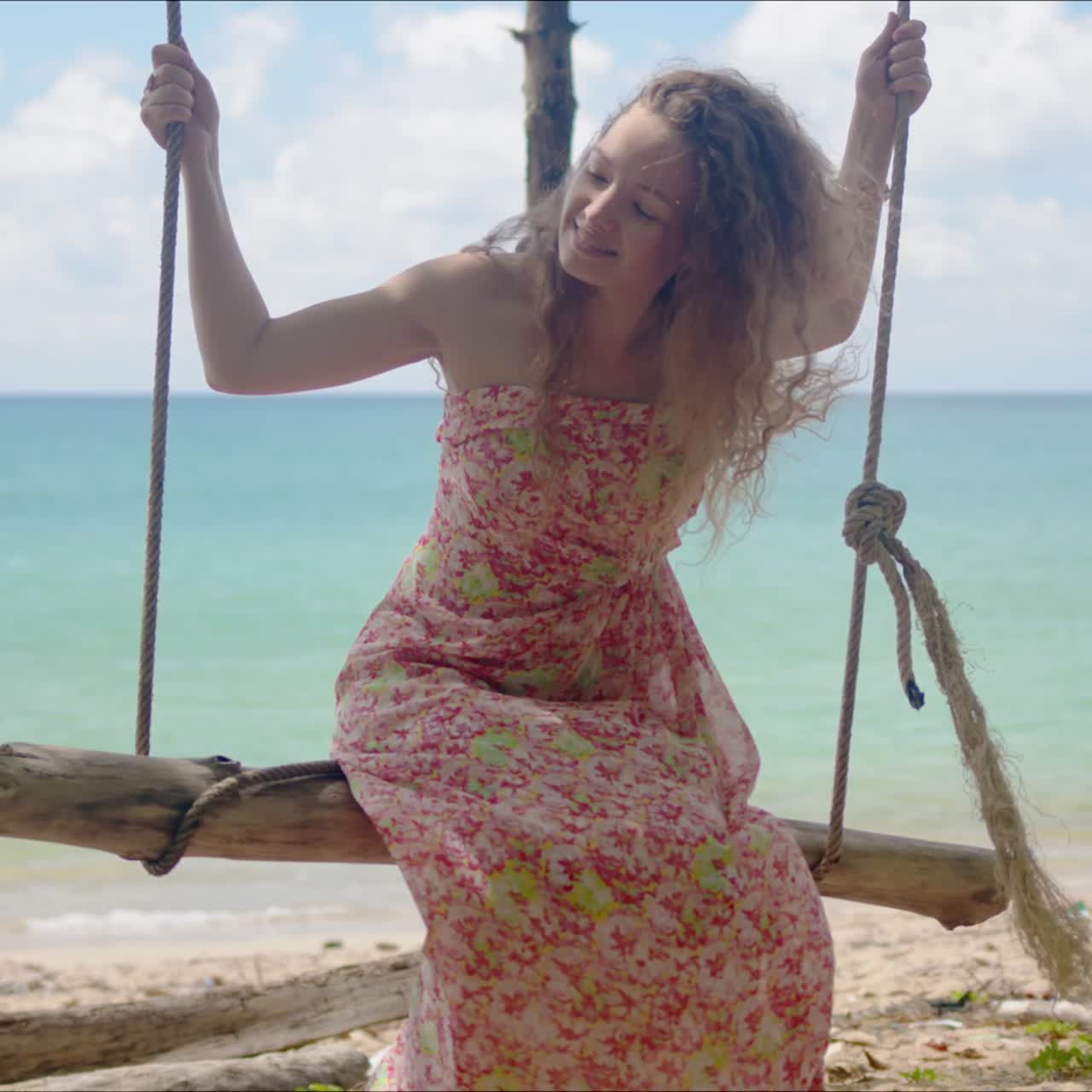 mujer alegre montando un columpio hecho a sí mismo en la playa