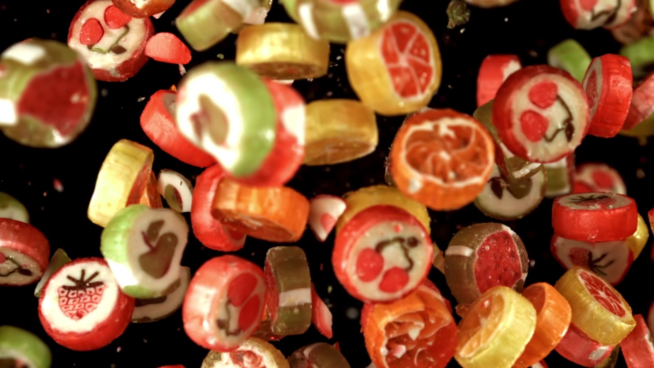 Bunte Fruchtbonbons fallen in Zeitlupe auf schwarzem Hintergrund
