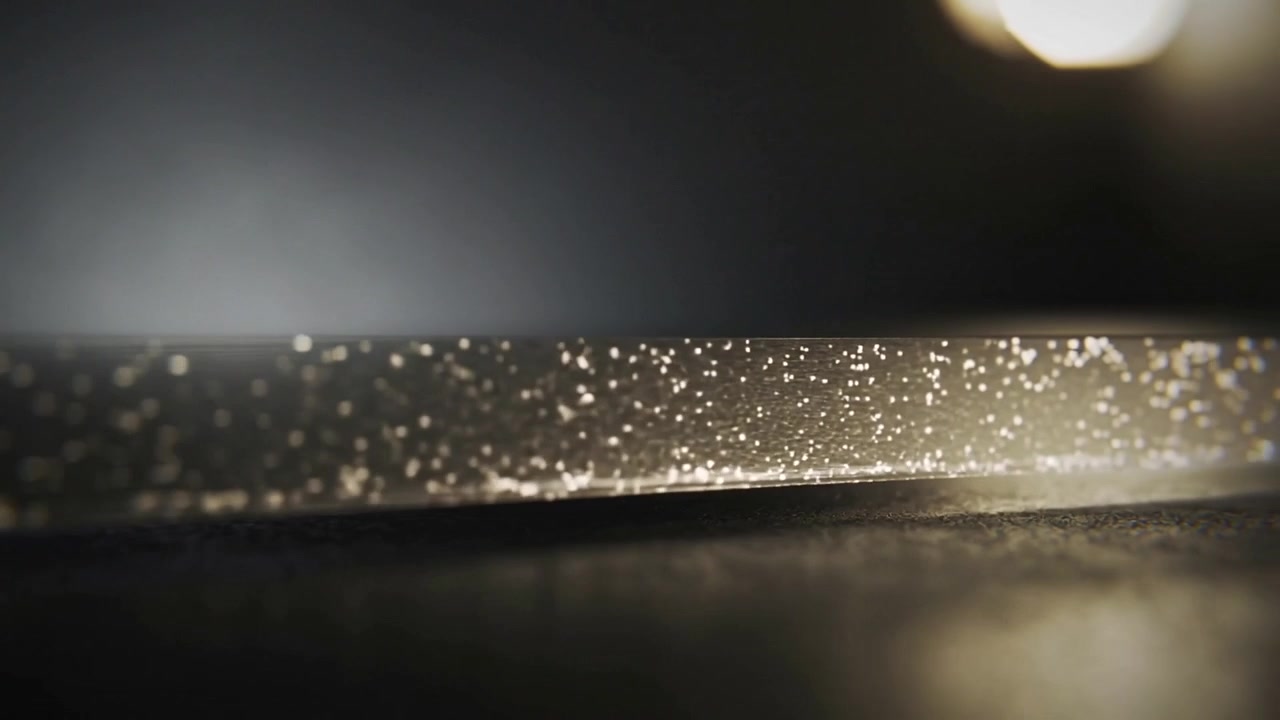 La telecamera mette a fuoco una stretta striscia di vetro su un tavolo da studio, mostrando macchioline scintillanti e bokeh.