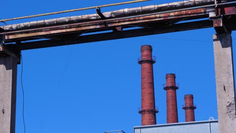 Exterior-view-of-abandoned-Soviet-heavy-metallurgy-melting-factory-Liepajas-Metalurgs-territory,-rust-covered-heat-pipelines,-distant-red-brick-chimneys-sunny-day,-medium-shot
