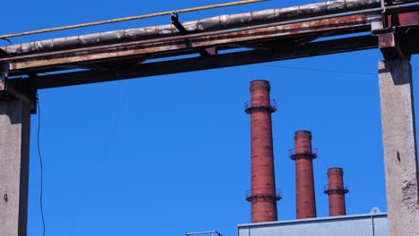 exterior view of abandoned soviet heavy metallurgy melting factory liepajas metalurgs territory, rust-covered heat pipelines, distant red brick chimneys sunny day, medium shot