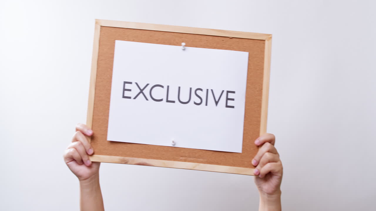 Woman's hand shows the paper on board with the word EXCLUSIVE in white studio background with copy space