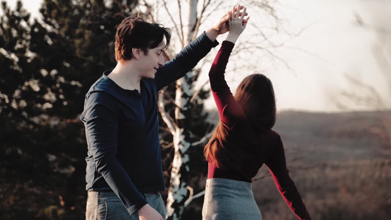 Lovely couple dance rotating pirouette at moody sunset on a mountain and having fun