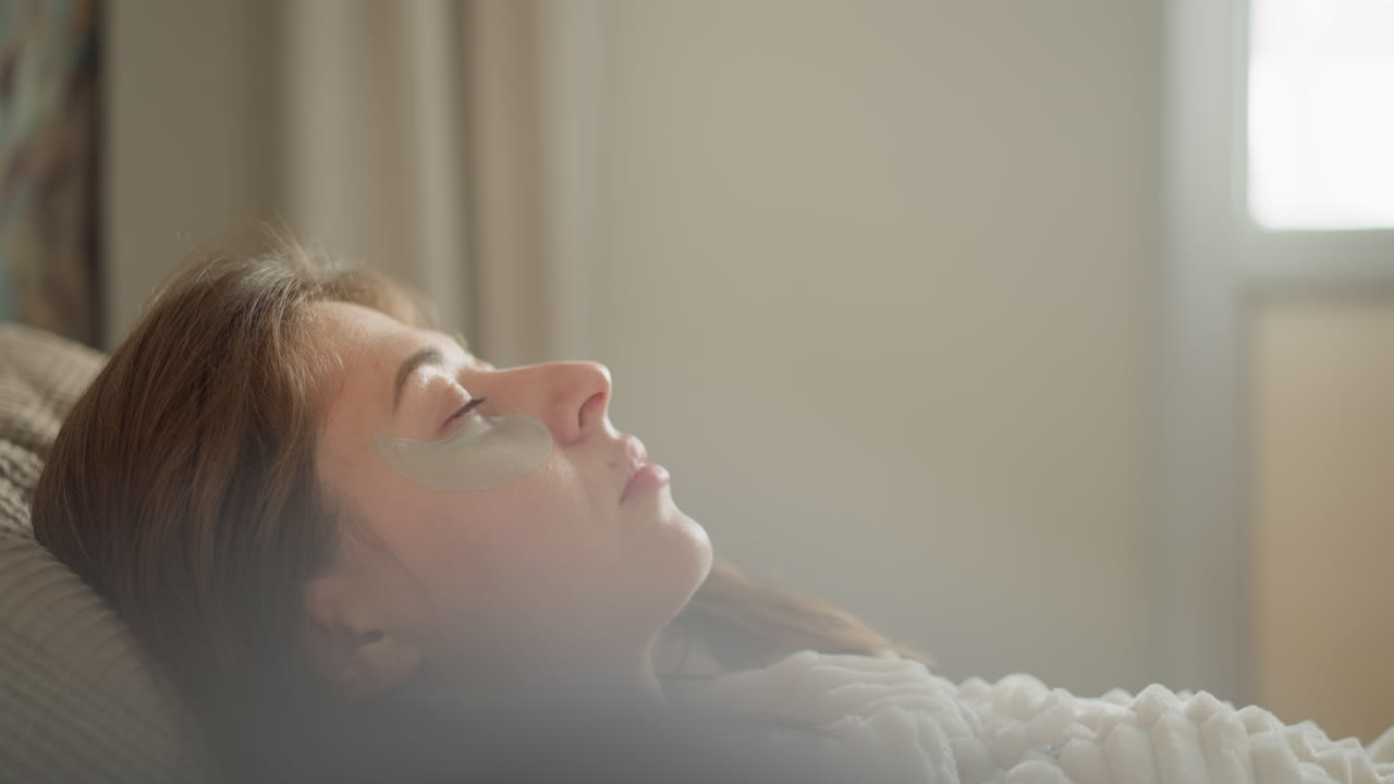 스파 치료 후 시간을 즐기는 갈색 여성은 침대에 누워있는 눈을 닫고 편안한 표정과 평온한 감정으로 베개에 누워 있습니다.