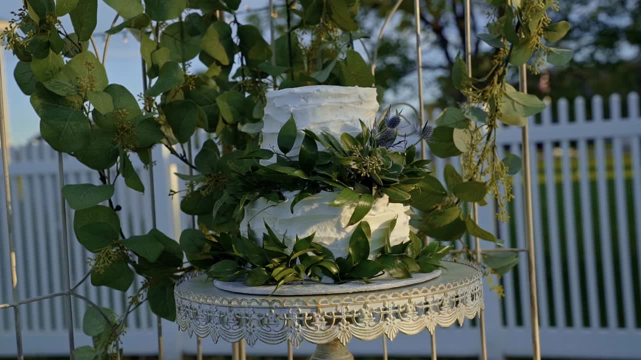 White wedding cake covered in green leaves at an outdoor summer wedding reception