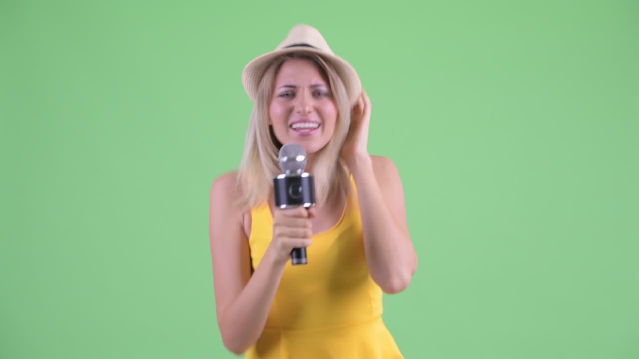 젊은 관광 여성이 초록색 배경에 마이크로 춤추고 노래하는 스튜디오