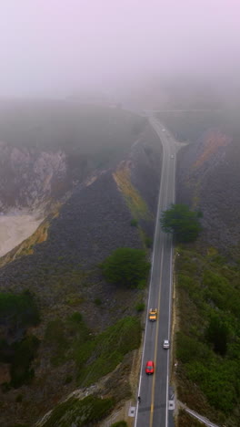 highway in the mountains with cars running by. beautiful rocks of montara, california, usa. horizon in thick fog. vertical video