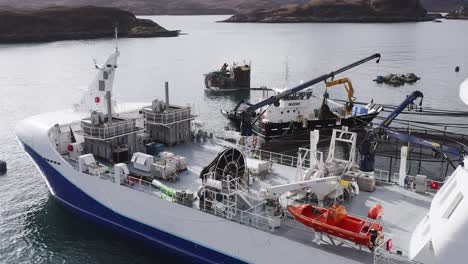 static drone shot of a well-boat using a crane to maintain a fish farm