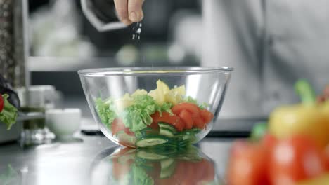 Chef-man-salting-salad-at-kitchen-restaurant.-Closeup-hand-salting-vegetables.