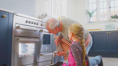 grandfather and granddaughter take freshly baked cupcakes out of the oven in kitchen at home