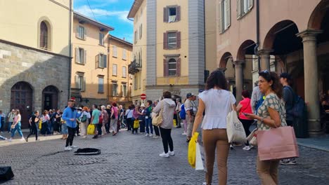 violinist busking on public square in the old town of bergamo, italy. tourists and locals passing and listening to his music on a sunny day