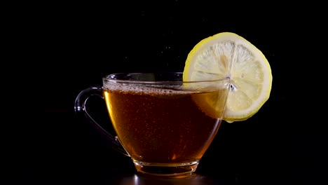 a stream of tea fills a glass cup with a lemon slice, set against a dark background
