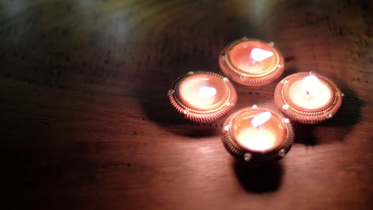 Panning right to traditional Indian light wax candles diya lit with flame and dance of shadow on wooden table during the celebration of Hindu festival of lights or Diwali or Deepawali.