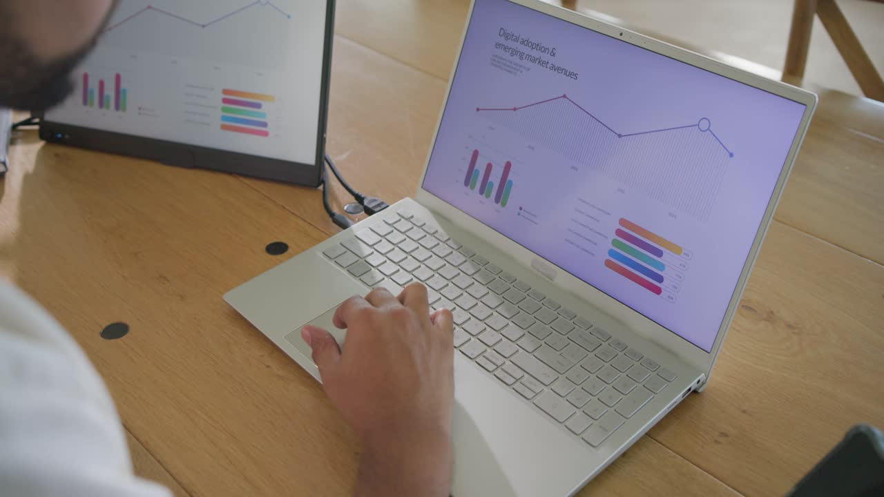 Man sitting left at wooden table, after chart update tapping and typing on laptop, copy space