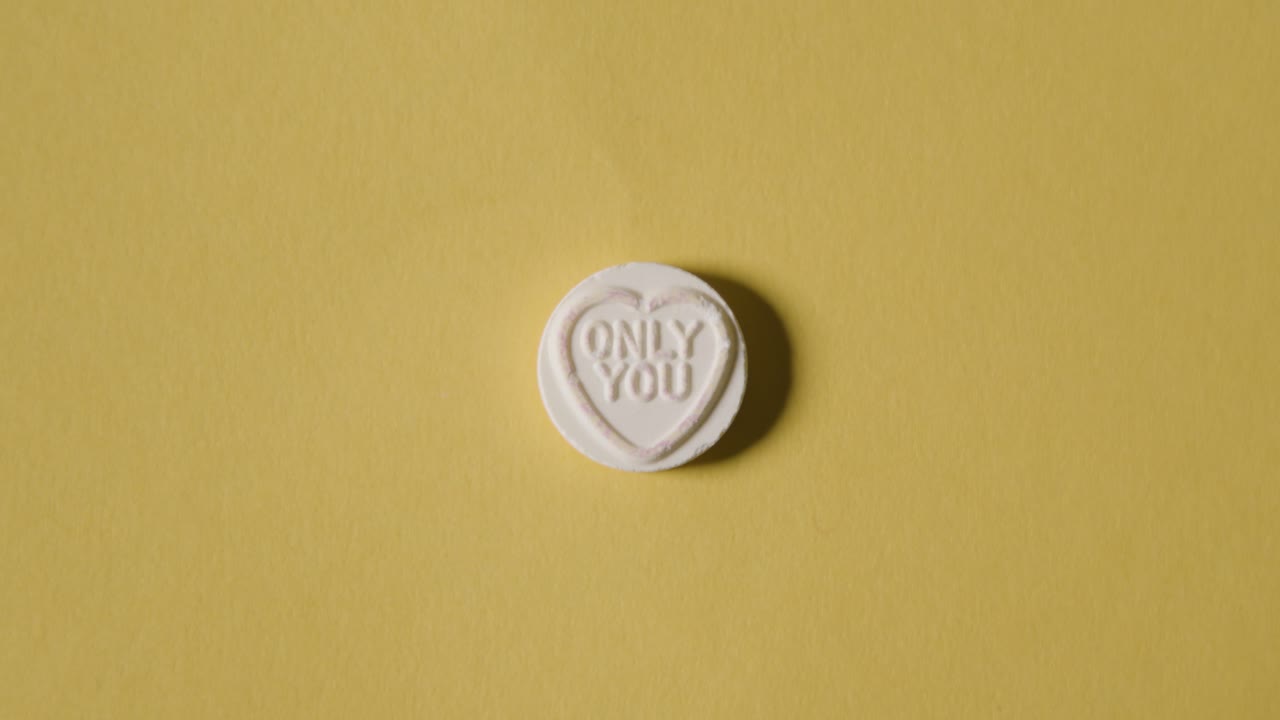 노란색 배경에 메시지만 있는 하트 사탕을 손에 들고