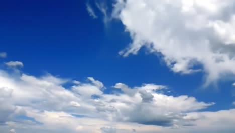 Large, fluffy clouds drift across a vivid blue sky, creating a peaceful atmosphere on a beautiful day. The sun casts bright light, enhancing the colors of the sky.