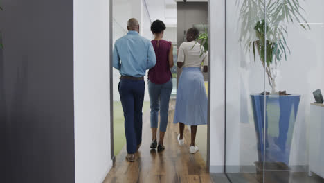 rear view of african american business people talking and walking in office corridor, in slow motion