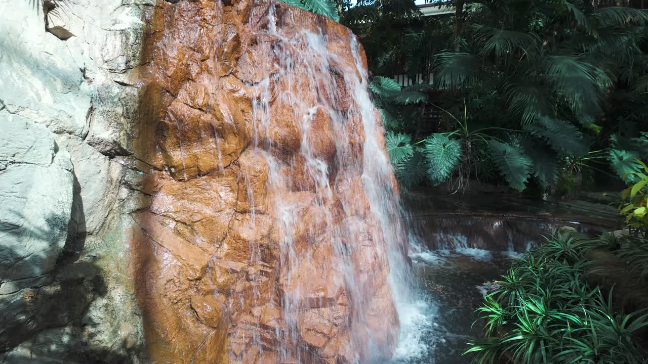 A close-up shot of clear water gently running over a smooth rock surface, flowing into a calm indoor pool.