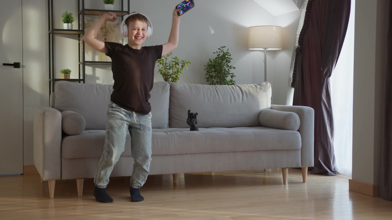 Young boy wearing headphones joyfully dances in living room moving energetically to music the