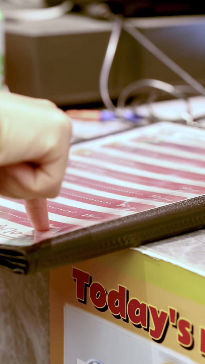 Close-up of customer hand tapping laminated menu at restaurant counter with electronic register