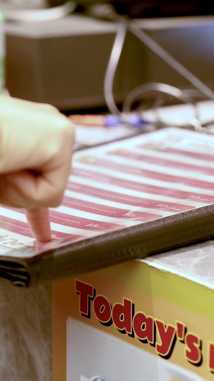 Close-up of customer hand tapping laminated menu at restaurant counter with electronic register