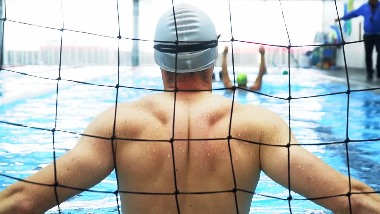 등이 강한 남자 수구 선수가 라이벌 팀의 공격을 위해 골대를 기다리고 있다