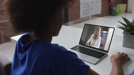 Rückansicht-Einer-Afroamerikanischen-Frau,-Die-Im-Büro-Einen-Videoanruf-Mit-Einer-Kollegin-Auf-Einem-Laptop-Führt