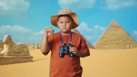 asian boy with a hat showing thumbs down gesture after looking through the binoculars. boy researcher examines something while traveling in giza pyramid, travel tourism adventure concept