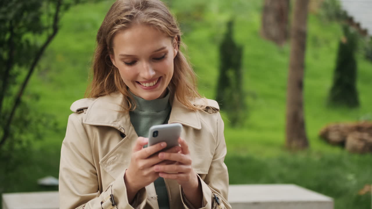 Caucasian female student using smartphone and smiling outdoors.