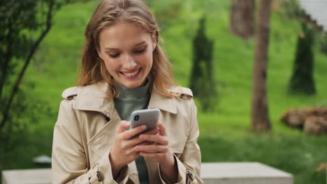 Kaukasische-Studentin-Benutzt-Smartphone-Und-Lächelt-Im-Freien.