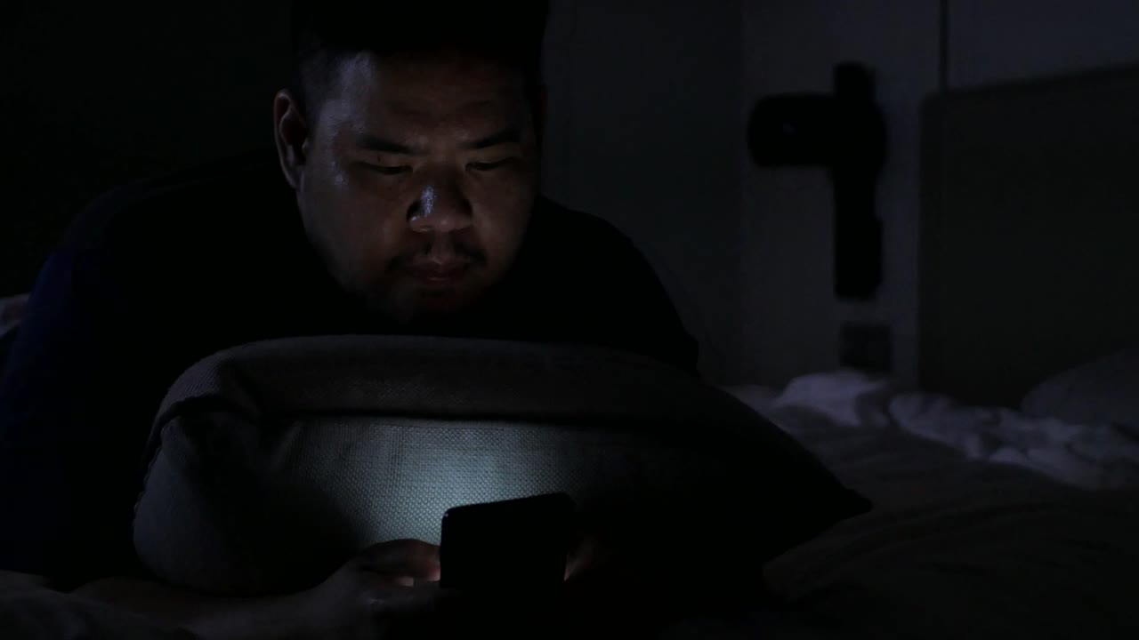 휴대 전화로 채팅하는 동안 아시아 남자와 밤 시간에 침실에서 침대에 누워
