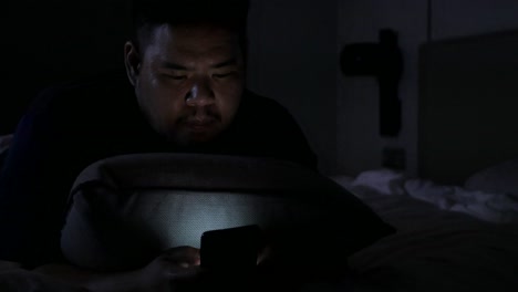 휴대 전화로 채팅하는 동안 아시아 남자와 밤 시간에 침실에서 침대에 누워