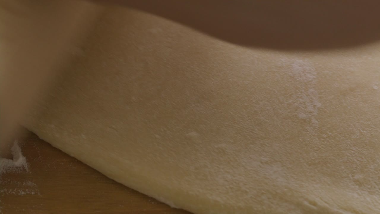 Hands of Baker Rolling Dough with Rolling Pin on Wooden Table
