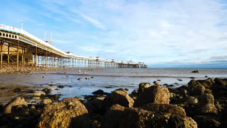 Sunny-Llandudno-Victorian-wooden-pier-ocean-view-across-rock-shoreline-dolly-right-slow