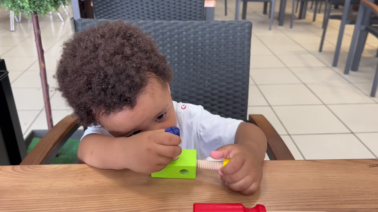 adorable niño afroeuropeo de dos años concentrado jugando con sus herramientas de juguete en una mesa