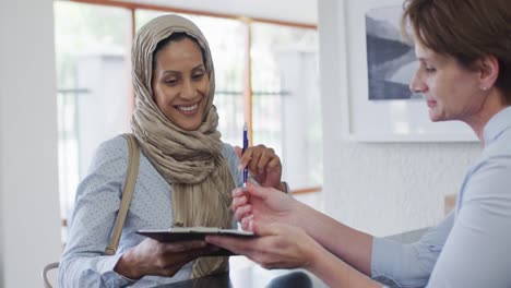 Smiling-biracial-woman-talking-and-signing-documents-at-reception-at-modern-dental-clinic