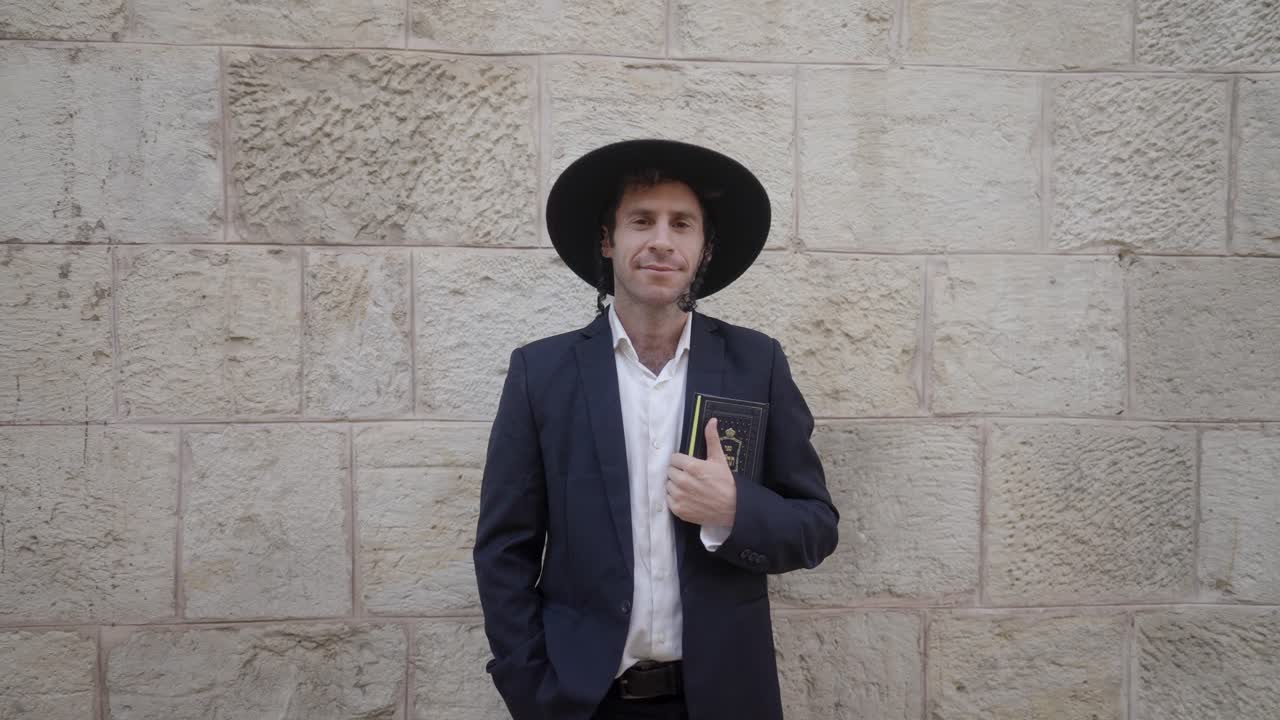 Confident Orthodox Jew holding a Tehillim, an ancient wall is behind him, in the Old City of Jerusalem, Israel