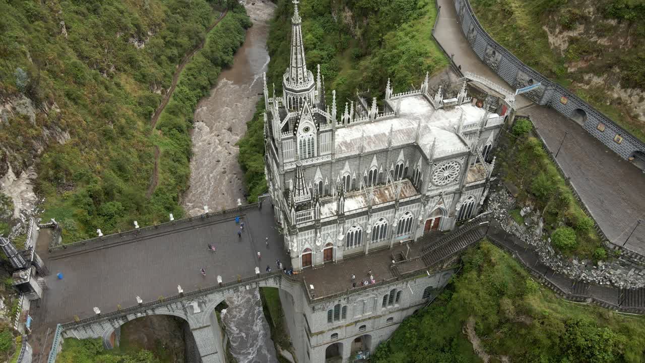 Aerial establishing orbit of Las Lajas Sanctuary spanning a lush canyon in Ipiales, Colombia, surrounded by greenery with rushing river below