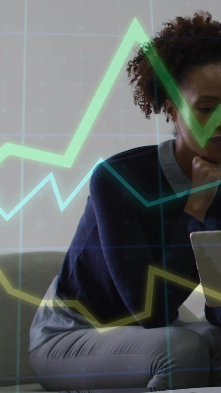 Vertical video: Woman on sofa tapping tablet causing finance charts overlay while making decisions