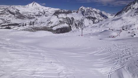 Vista-De-Drones-De-Hermosas-Montañas-Con-Esquiadores---Tiro-Inclinado-Hacia-Arriba-Y-Carro-En-Tiro---Tiro-En-Tignes-Y-Val-D&#39;isere