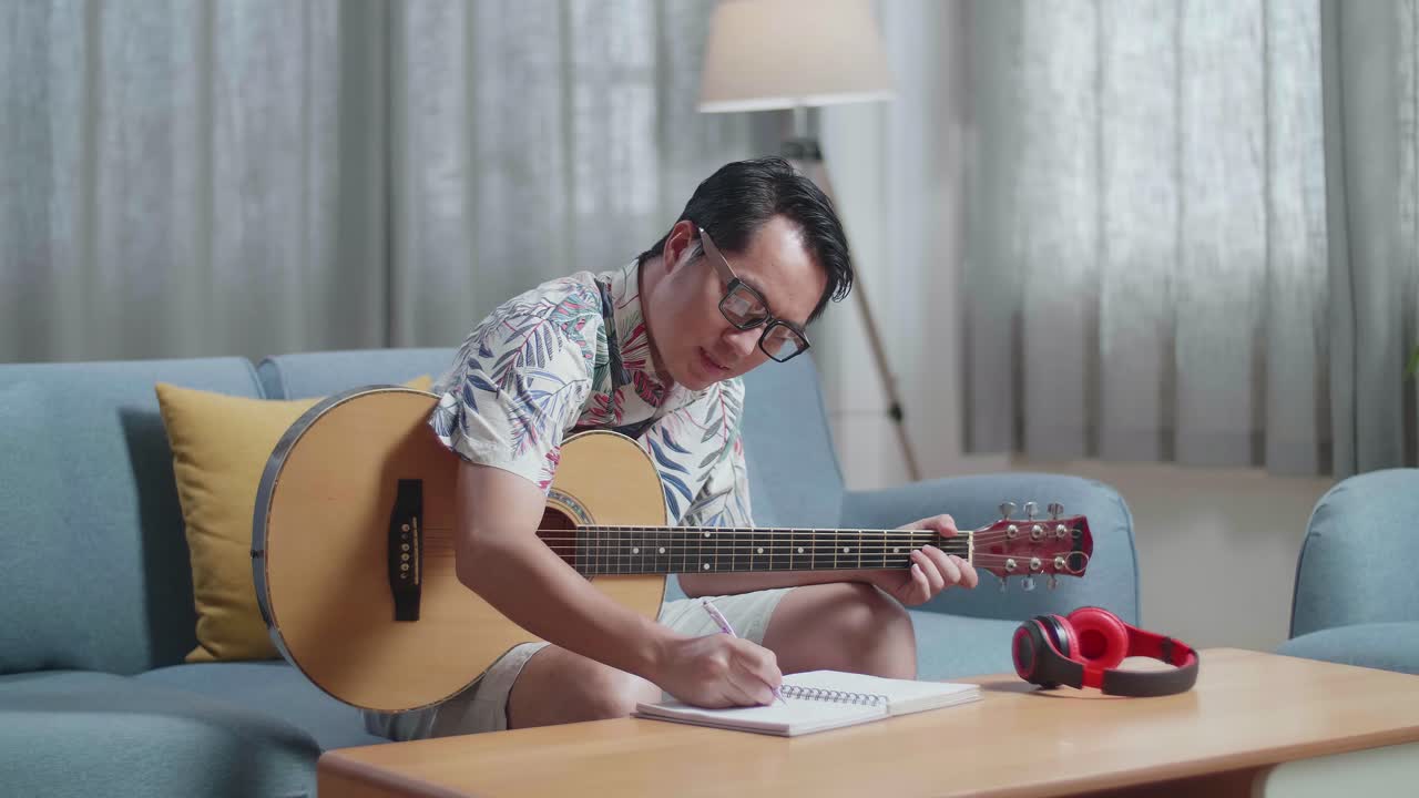 Compositore asiatico con una chitarra che festeggia per aver finito di comporre musica su carta a casa
