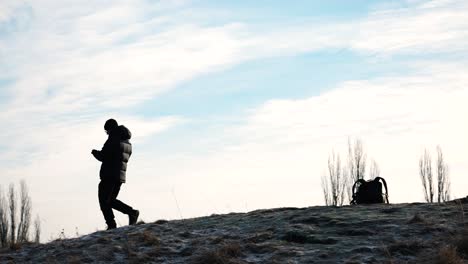 person in black jacket walk on rocky hill and leave backpack, drone follow