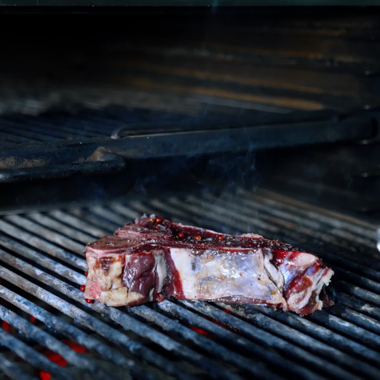 Piece of beef is put on the grill with the help of tongs. Cooking meat on the charcoals. Vertical screen