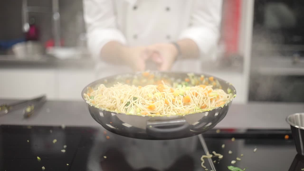 전문 요리사가 요리 워크 ⁇ 에서 다민족 학생들에게 팬에 재료를 던지는 기술을 보여줍니다.