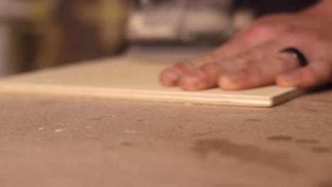 close up of a sander power tool smoothing down a square of softwood with a carpenter's hand holding it steady