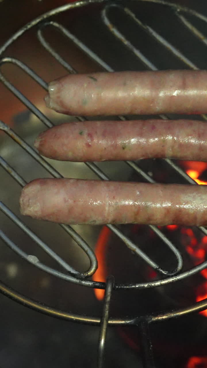 Close-up of sizzling sausages on a flaming grill, showcasing juicy texture and savory aroma. Perfect for BBQ concepts. Captured in vivid detail, ideal for vertical video use