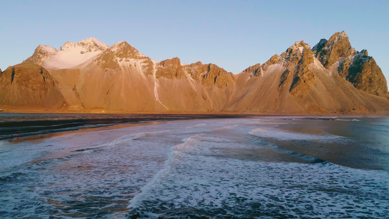 Gylden solopgang over Vestrahorn-bjerget og Stokksnes-stranden med skummende havbølger, luftfoto over kystlinjen.