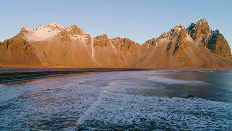 Golden-sunrise-Vestrahorn-Mountain-and-Stokksnes-beach-foaming-ocean-waves,-Aerial-view-over-coastline